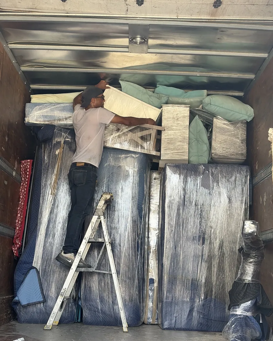 A Stack Haus mover on a step ladder stacking wrapped furniture up to the ceiling of the truck