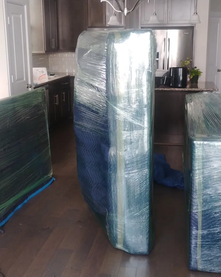 Furniture padded with blue moving blankets and shrink-wrapped in a kitchen, ready to load